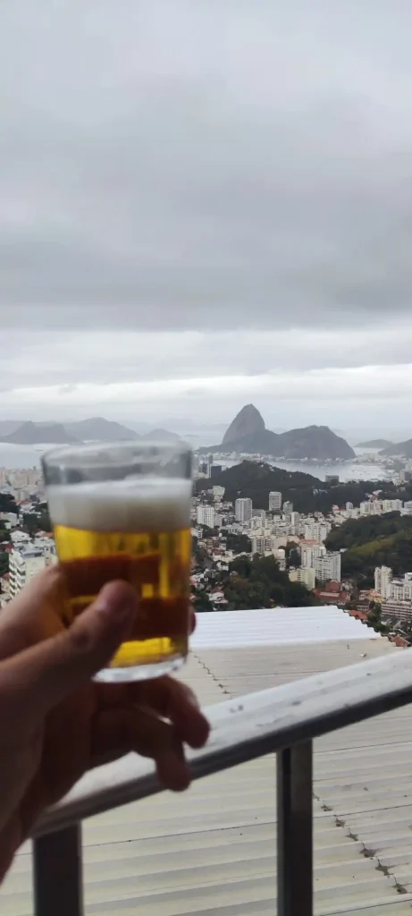 Vaso de cerveza lager fría sostenido en primer plano con vistas desenfocadas y nubladas del Pan de Azúcar de fondo.