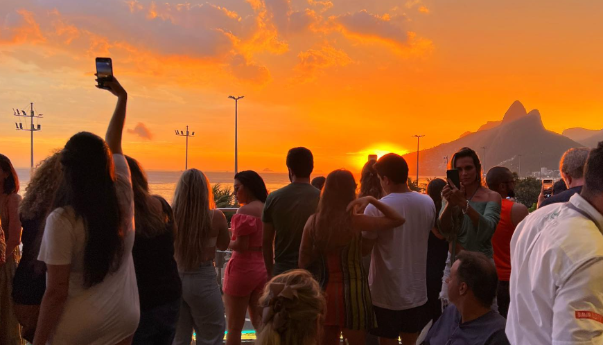Gente disfrutando del atardecer en la terraza del Boteco Belmonte Ipanema con vistas al Morro Dois Irmãos.
