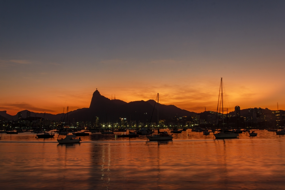 Puesta de sol desde la Mureta da Urca en Río de Janeiro, mostrando la silueta del Cristo Corcovado y barcos en la Bahía de Guanabara.