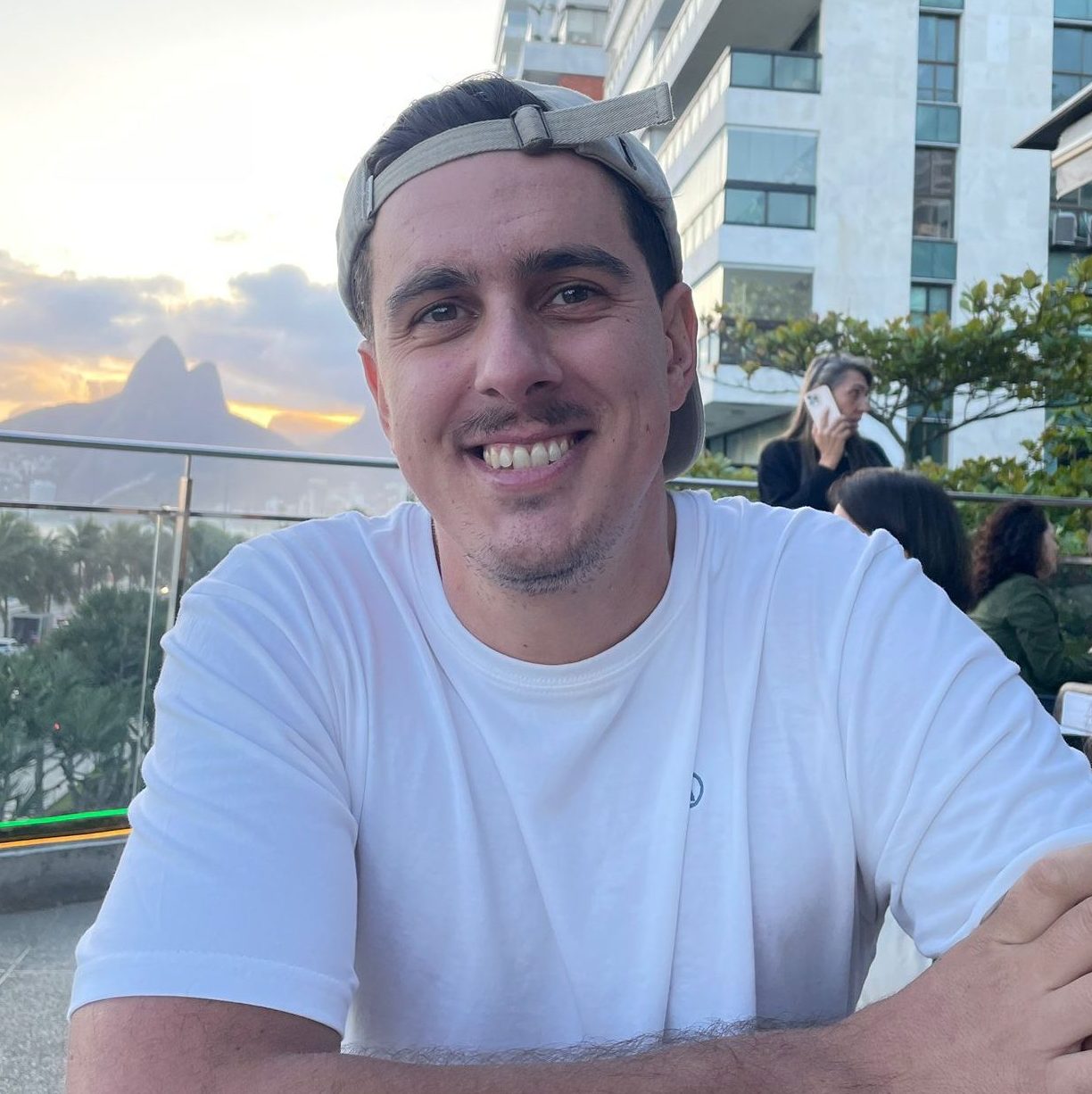 Antonio, autor de Río de Verdad, sonriendo en un atardecer en Río de Janeiro con el Morro Dois Irmãos de fondo.