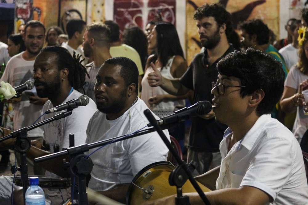 Primer plano de un músico tocando un pandeiro rojo con la imagen de San Juan Bautista durante una roda de samba en la Pedra do Sal, Río de Janeiro.