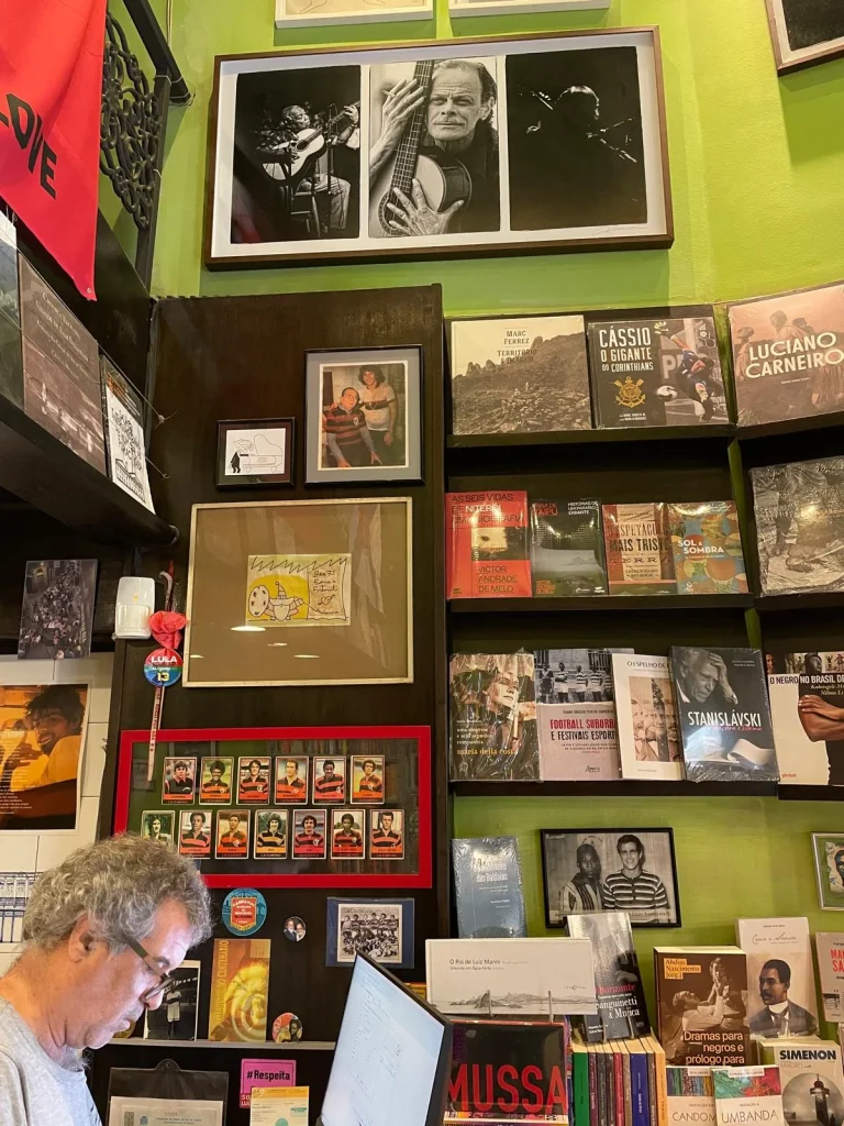 Estanterías interiores de la Livraria Folha Seca en Río de Janeiro, mostrando cuadros de músicos de samba, libros de fútbol brasileño y una colección enmarcada de cromos antiguos del club Flamengo.