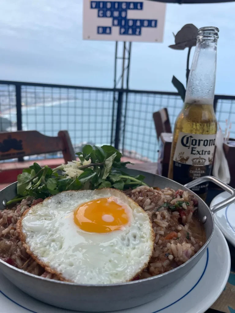 Arroz de costela con trozos de carne y huevo frito servido en una terraza del Mirante do Arvrão con vistas al mar y al Morro Dois Irmãos en Río de Janeiro.
