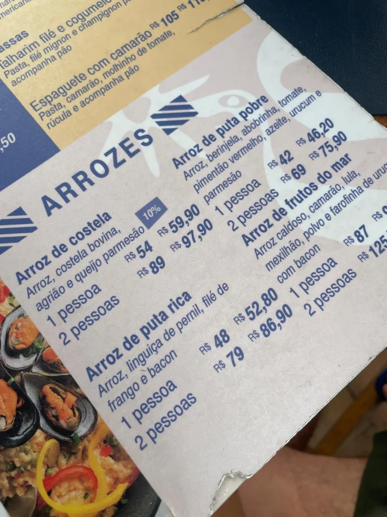 Fotografía en primer plano de la sección de arroces de la carta del restaurante en Vidigal, donde aparecen los platos Arroz de costela, Arroz de puta rica y Arroz de puta pobre con sus respectivos precios en reales.
