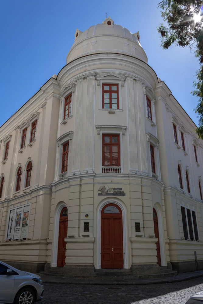 Fachada neoclásica del Centro Cultural Correios en el Centro de Río de Janeiro, mostrando su entrada principal en esquina, ventanas de madera marrón y su característica cúpula blanca bajo un cielo despejado.