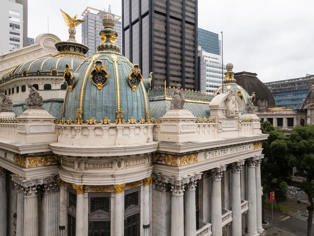 Fachada e imponente cúpula dorada del Theatro Municipal de Río de Janeiro en la plaza de Cinelândia bajo un cielo azul despejado.