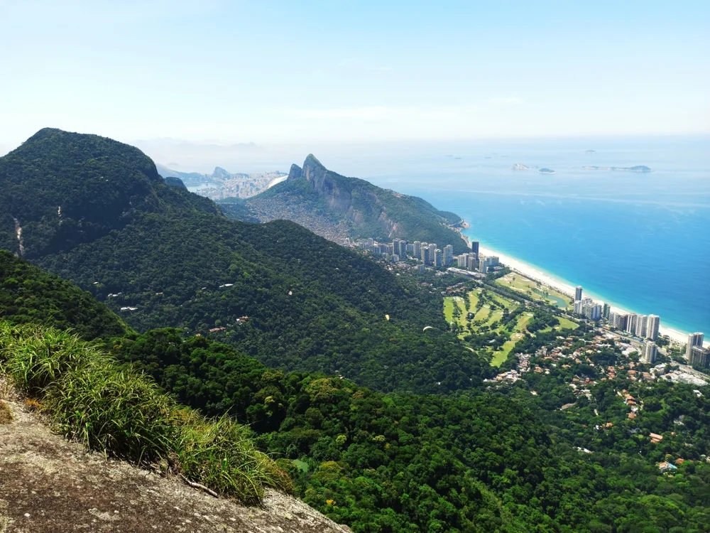 Vistas panorámicas de Río de Janeiro desde el mirador de Pedra Bonita. Se aprecia la densa selva atlántica del Parque Nacional de Tijuca, el morro Dois Irmãos y la favela Rocinha al fondo, junto a la costa turquesa de São Conrado.